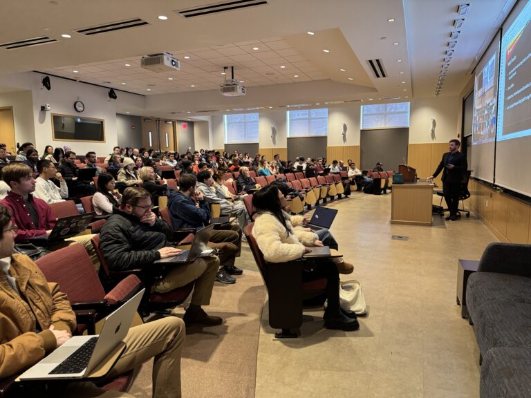 A full lecture hall of students with laptops listening to a speaker present slides at the front of the room during a WashU Law program on artificial intelligence and the practice of law.