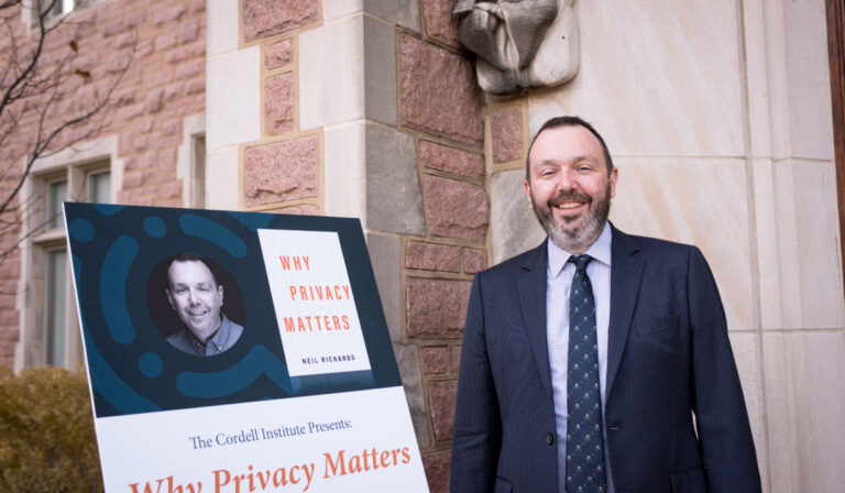 Neil Richards in a dark suit smiling next to a Cordell Institute event sign promoting his book "Why Privacy Matters," displayed outside a stone building.