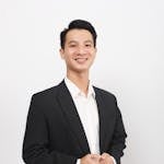 Portrait of a smiling man in a black suit with a white background, conveying confidence and professionalism.
